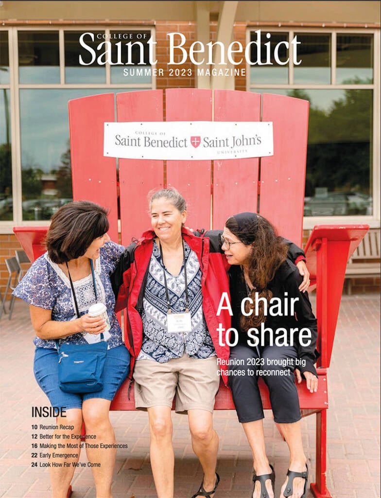 Three women sit smiling on a large red chair outside a building. They're wearing casual clothing, and each has a name badge around their neck. The background shows a sign for the College of Saint Benedict. Text on the image references a 2023 reunion.