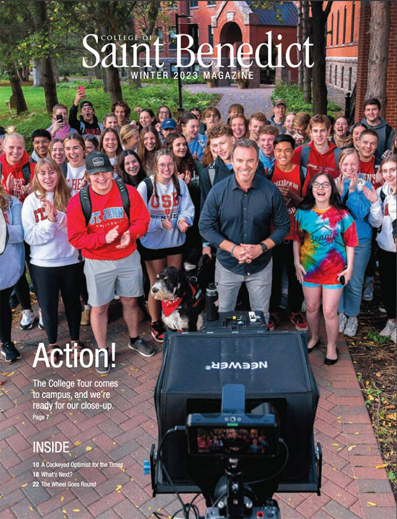 A group of smiling college students and a man stand outdoors in front of a brick building. The students wear casual clothes, and a camera is set up in front. The scene is from the "College of Saint Benedict Winter 2023 Magazine.