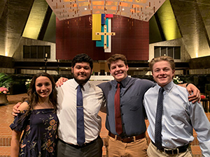 Group of male and female students arm and arm in a church standing in a row smiling