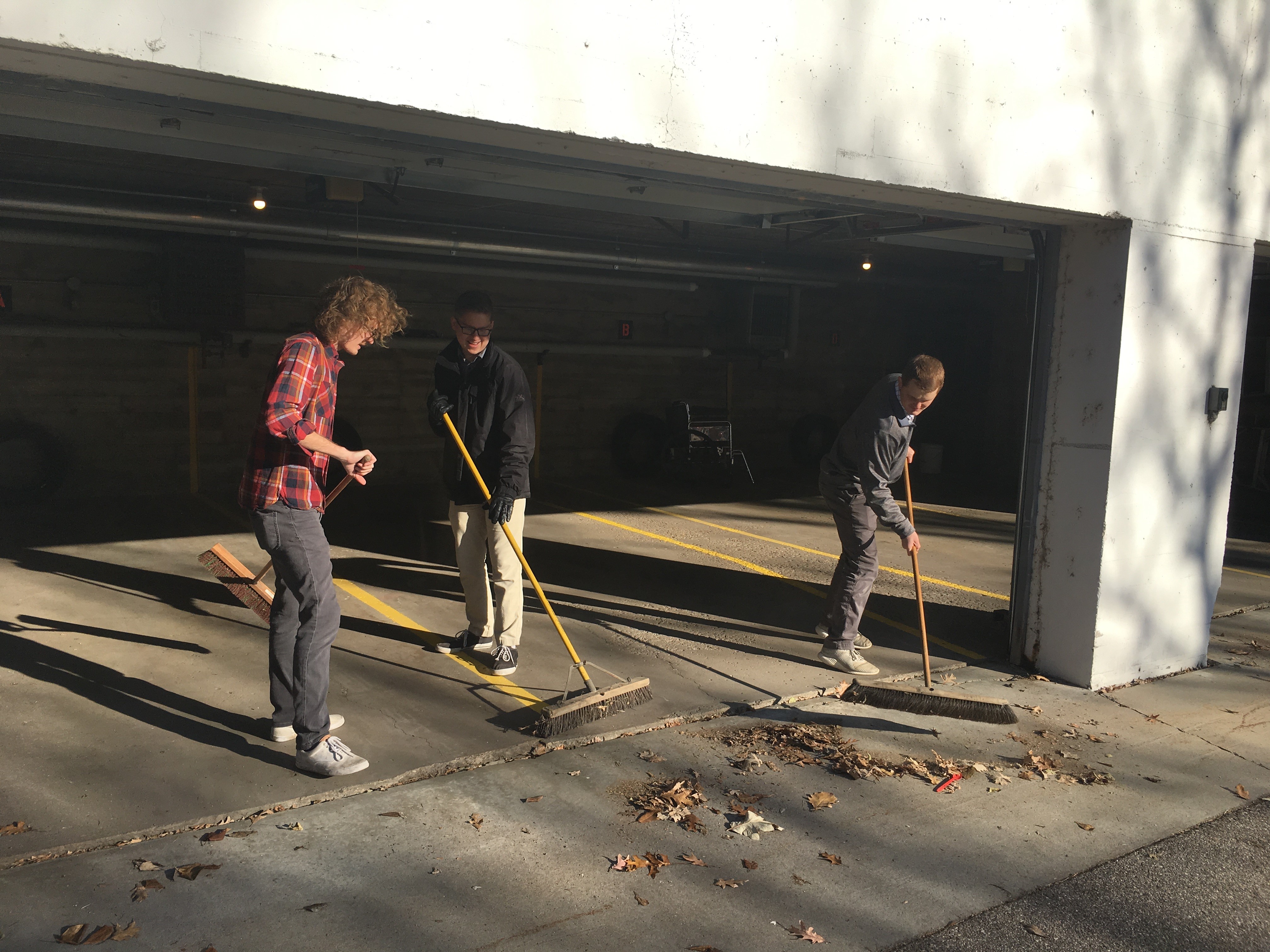 Three college students working to clear out a garage area in the fall