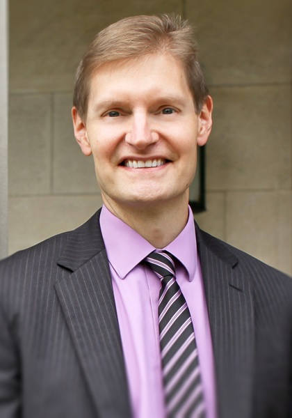 Man in grey suit with magenta shirt smiling