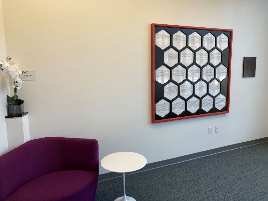 Image of an interior room with a chair and a framed work of art with honeycombs filled will text