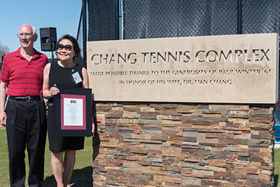 Photo of Paul Winter and his wife, Dr. Lian Chang by the Change Tennis Complex sign