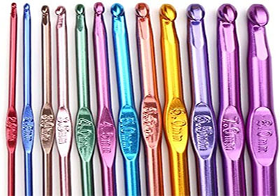 An array of colorful aluminum crochet hooks laid out in a row. The hooks range in size from small to large and are in various colors including red, pink, green, blue, purple, gold, and orange. Each hook has size markings engraved on the handle.