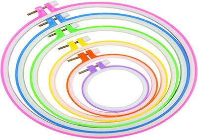 A set of seven circular embroidery hoops arranged in a nested manner, each hoop in a different vibrant color, including pink, green, blue, yellow, and orange. The hoops have metal screws on one side for tightening.