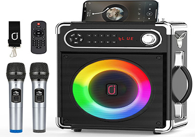 Portable karaoke machine with a multicolored LED display. It has two microphones, a remote control, and a strap. A smartphone is connected on top, showing a music app screen.