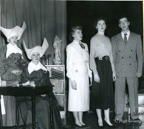 A vintage photo shows two people dressed as nuns seated at a table, next to three standing individuals in mid-20th century attire. A religious statue and bookshelf are in the background. The words "'52 High Ground" are in the bottom right corner.