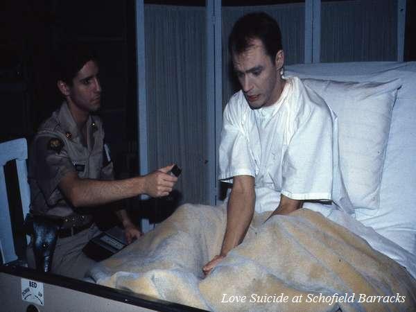 A man in a hospital bed, sitting with a pensive expression, is being interviewed by a man in a military uniform holding a microphone. A blanket covers the man's lap. The image has a title in the corner: "Love Suicide at Schofield Barracks.