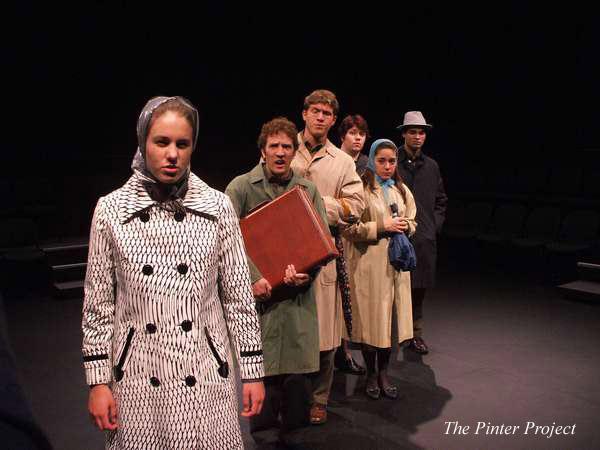 A group of six people in vintage attire, including coats and headscarves, stand in a line on a dark stage. The person at the front wears a patterned coat. The setting appears theatrical. Text reads "The Pinter Project" on the bottom right.