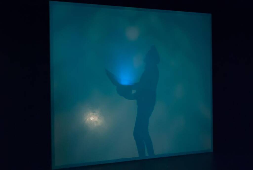 Silhouette of a person holding an open laptop, standing against a glowing blue background, creating a mysterious and futuristic atmosphere.