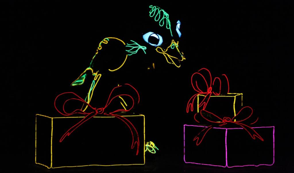 An animated neon bird with vibrant green, blue, and yellow lines, appears delighted as it looks at three neon-outlined gift boxes tied with red bows against a black background. The gifts vary in size and are brightly outlined in yellow, red, and purple.