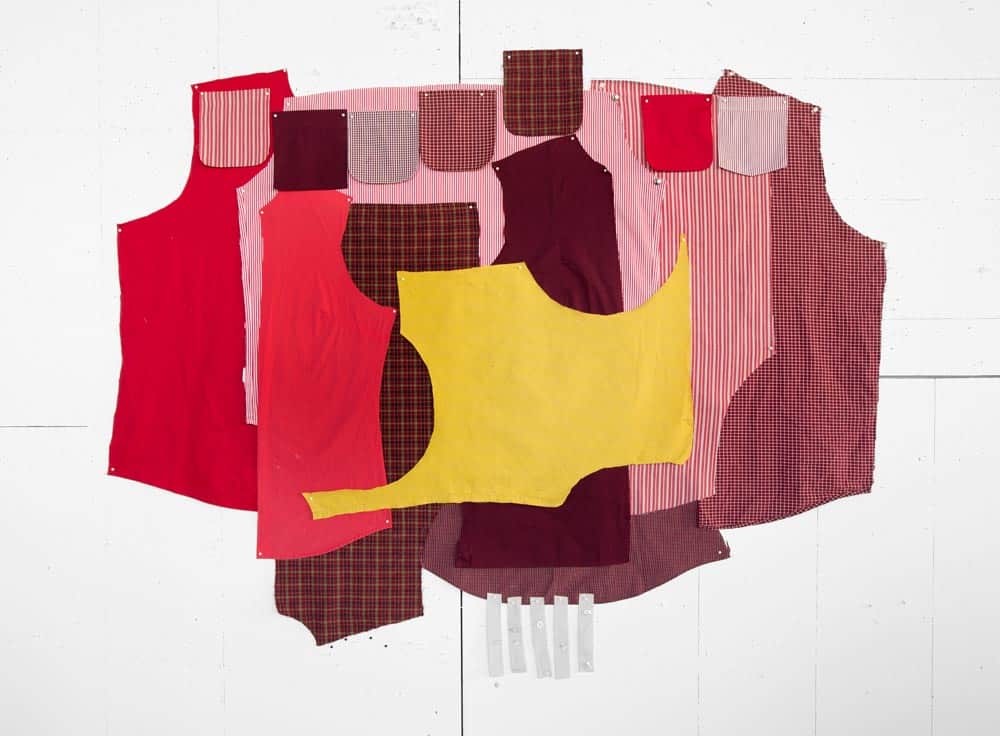 A collage of various fabric swatches in different patterns and colors, including red, yellow, pink, and maroon, cut into shirt-shaped pieces and overlapping each other against a plain white background.