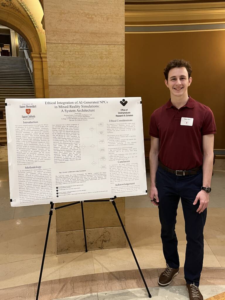 A person stands indoors next to a large poster presentation on ethical AI integration. They're wearing a maroon shirt and dark pants, smiling at the camera. The background features a staircase and stone architecture.